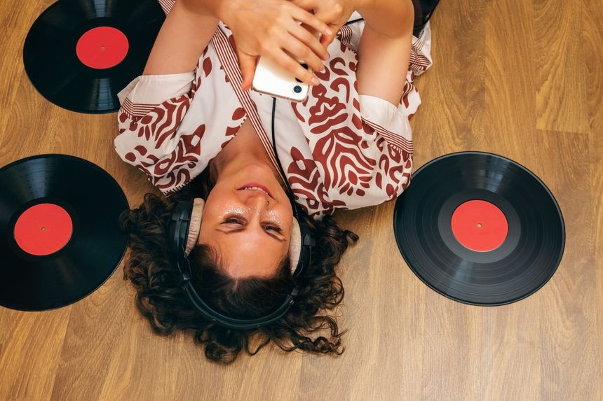 Woman lying on floor with headphones , vinyl records and phone.