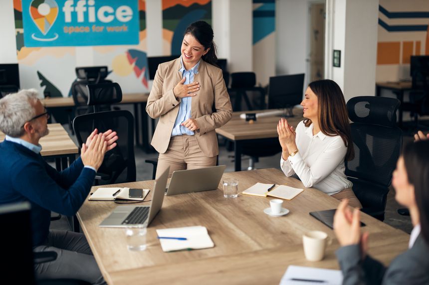 Colleagues celebrate and applaud a fellow employee in a modern office setting, showcasing teamwork.