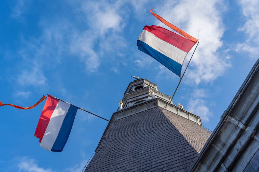 The National Flag of the Netherlands with orange pennant against the blue sky