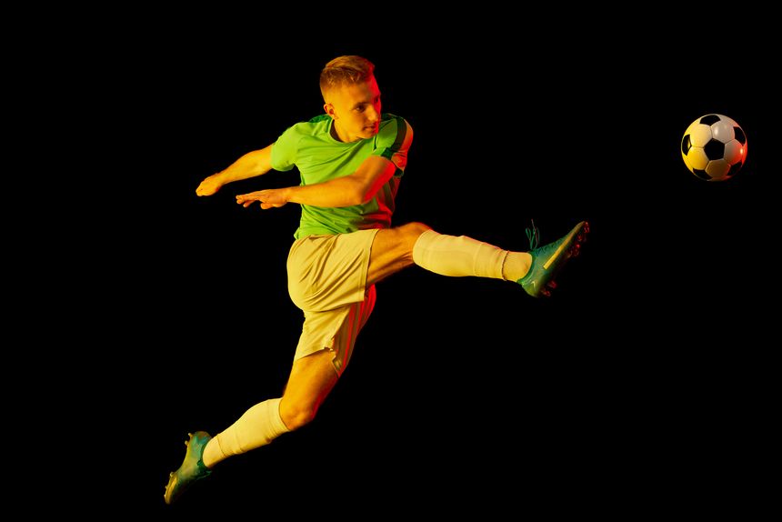 Leg kick. Young professional male football soccer player in motion and action isolated on dark background in neon light. Concept of sport, goals, competition, hobby, ad.
