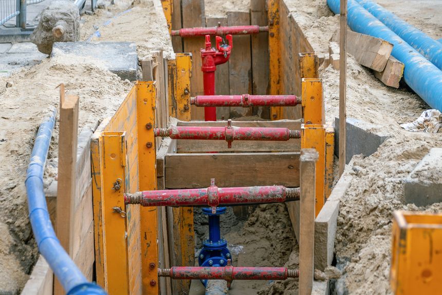 Construction site with colorful pipes and wooden supports in a trench.