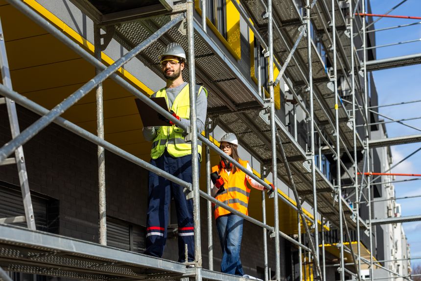 Two professional engineers in safety gear walking along construction scaffolding while surveying the building project. This image effectively captures the dynamic nature of field inspections and modern construction management.