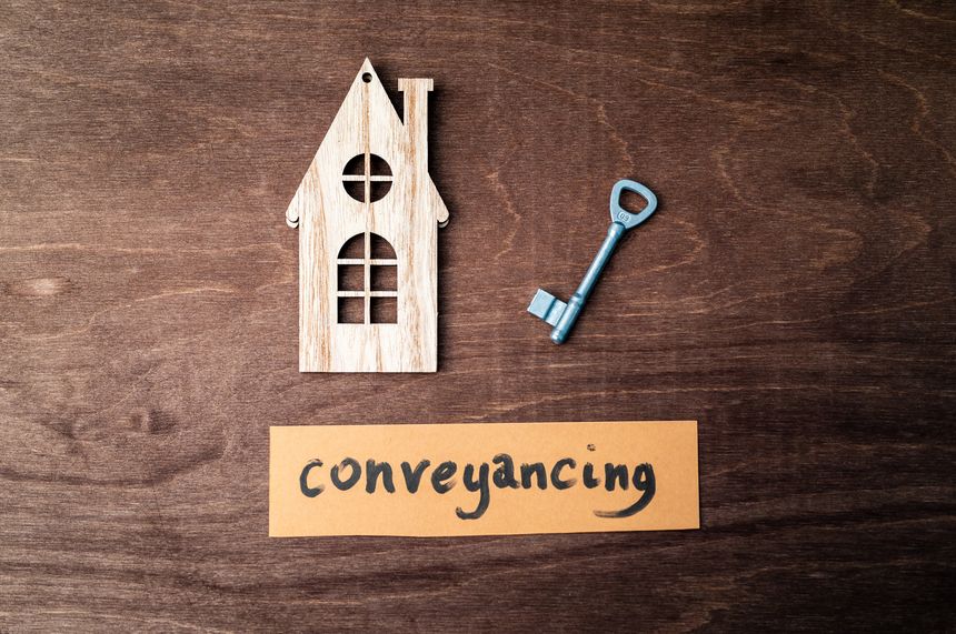 a cut out wooden house representation with a key and a card saying 'conveyancing' on wood background