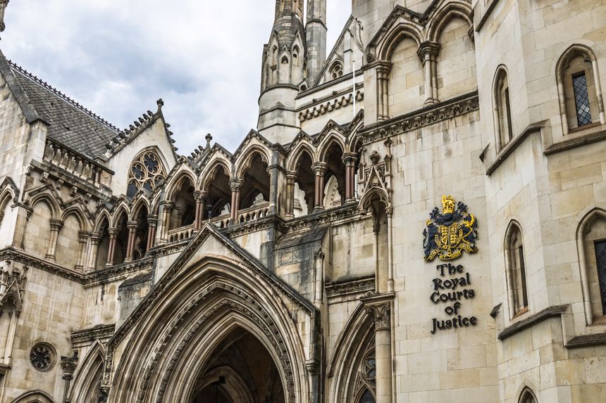 Low angle view of the Royal Courts of Justice on London Strand, ornate Victorian Gothic stonework and royal coat of arms under dramatic clouds. London, UK, 5 May 2024