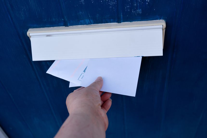 Close-up of a female hand inserting white envelopes into a letterbox door.