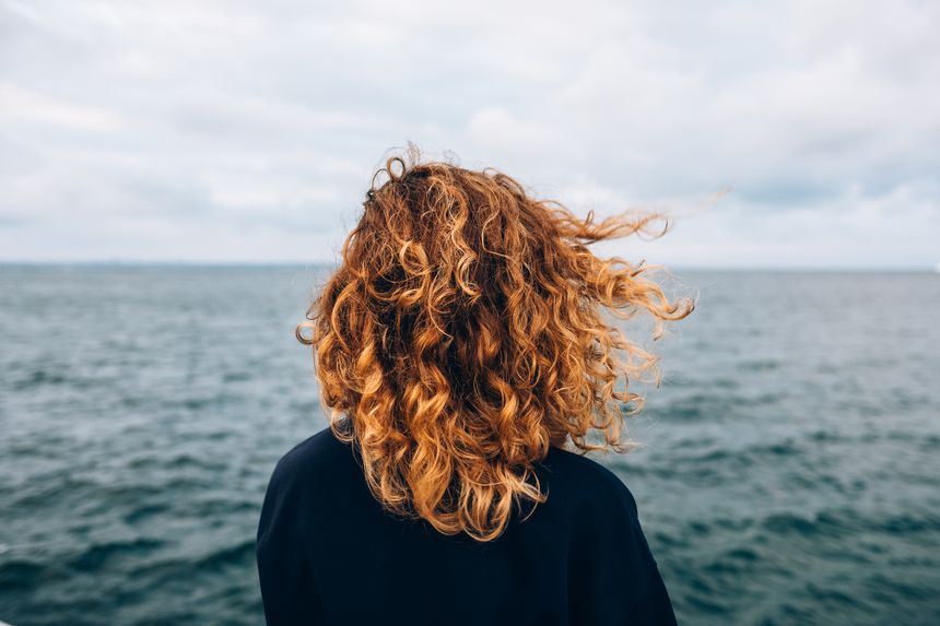 View from the back a woman with curly hair looks at the sea