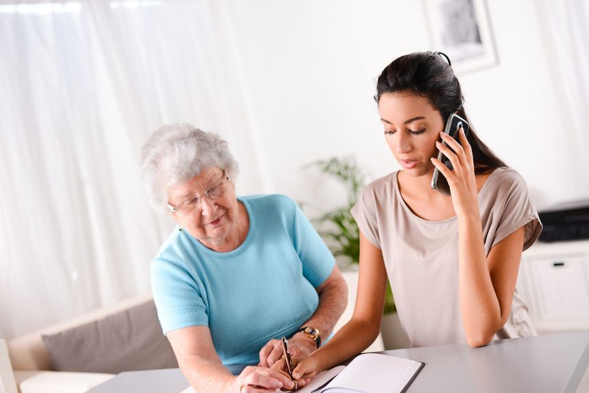 cheerful young woman helping an old person doing paperwork and telephone call