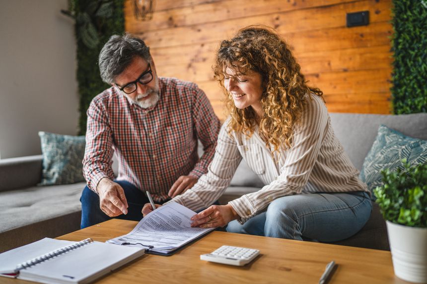 senior man instructs adult woman to sign contract, document at home