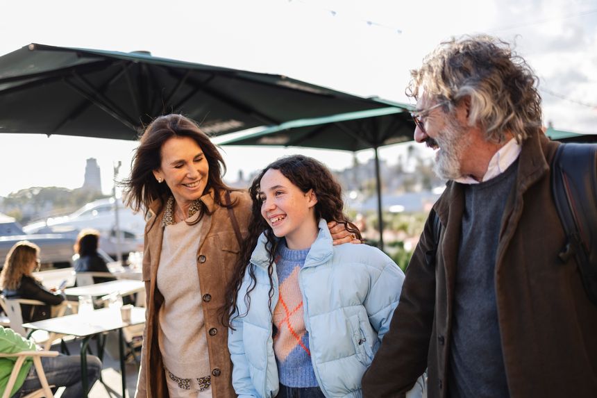 Happy family consisting of a mother, father, and daughter walking together outdoors in an urban environment, sharing smiles and warm hugs, embodying love and togetherness