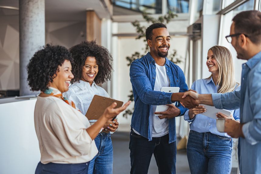 A diverse group of professionals smiling and shaking hands in a modern office environment. The image conveys teamwork, collaboration, and positive business relationships.