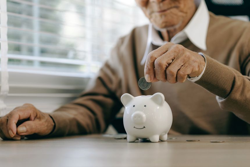 Saving money investment for future. old man hand putting money coins in a piggy bank.investment, money, annuity insurance, saving for retirement and pension fund concept.Individual retirement account.