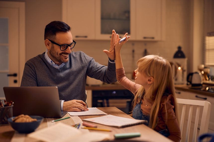 Happy little girl giving high-five to her father while he's working at home.