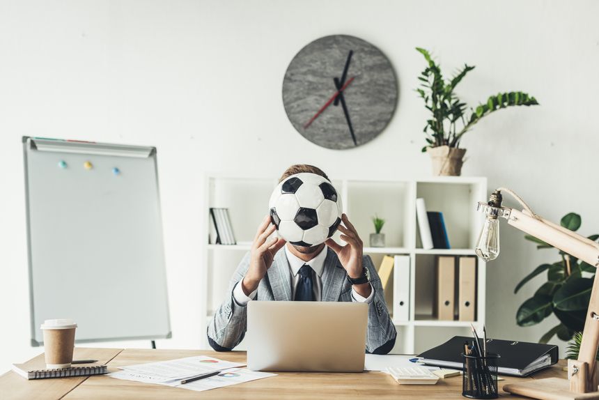 businessman covering face with soccer ball at modern office
