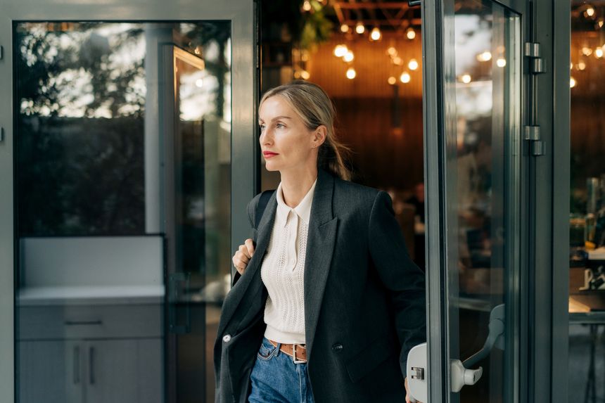 Businesswoman exits a modern restaurant, wearing blazer and white blouse, ready for the day