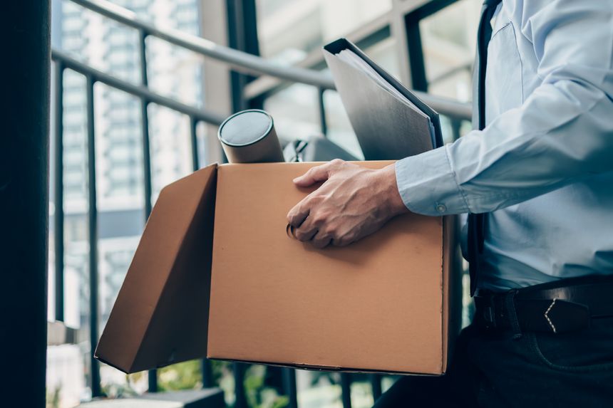 Unemployed hold cardboard box and laptop bag, dossier and drawing tube in box. Quitting a job, businessman fired or leave a job concept.