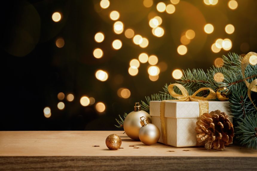 Holiday background with gift box, pine branches, cones and baubles on wooden table. Warm golden bokeh and copy space for greeting cards, banners and promotions.