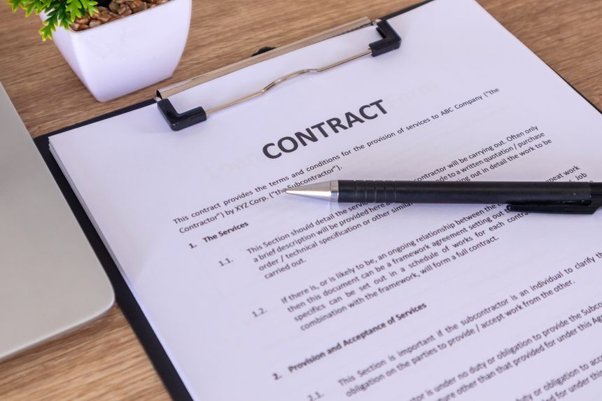 Contract documents on the wooden table with pen and laptop