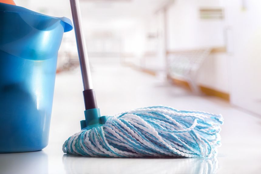 Mop with white and blue fibers and blue mop bucket on clean reflective floor in a white corridor. Front view.