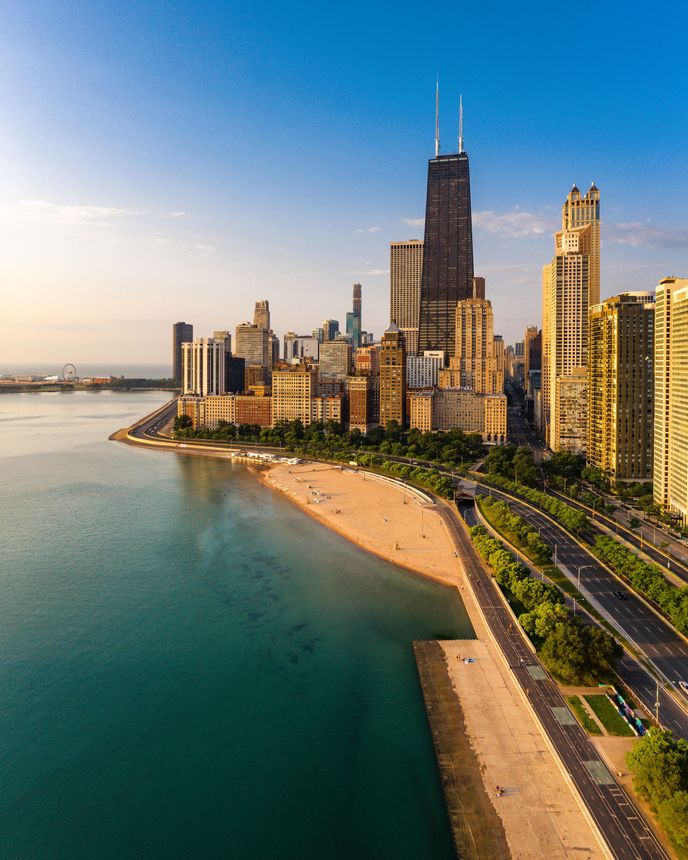 Aerial view of downtown Chicago with the John Hancock Center and Lake Michigan shoreline glowing at sunrise.