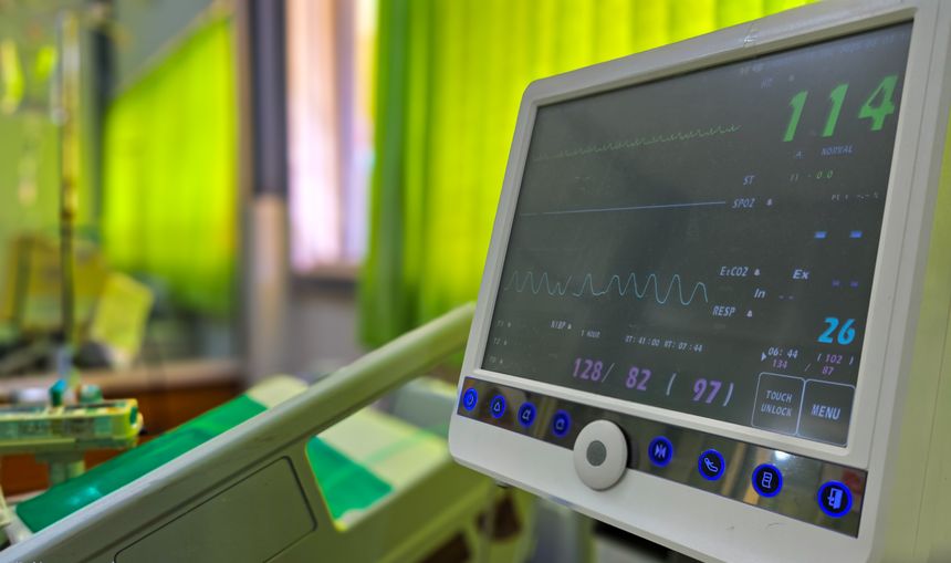 A close-up view of a modern vital signs monitor displaying patient data, including heart rate, blood pressure, and oxygen saturation, in a hospital room or intensive care unit (ICU).
