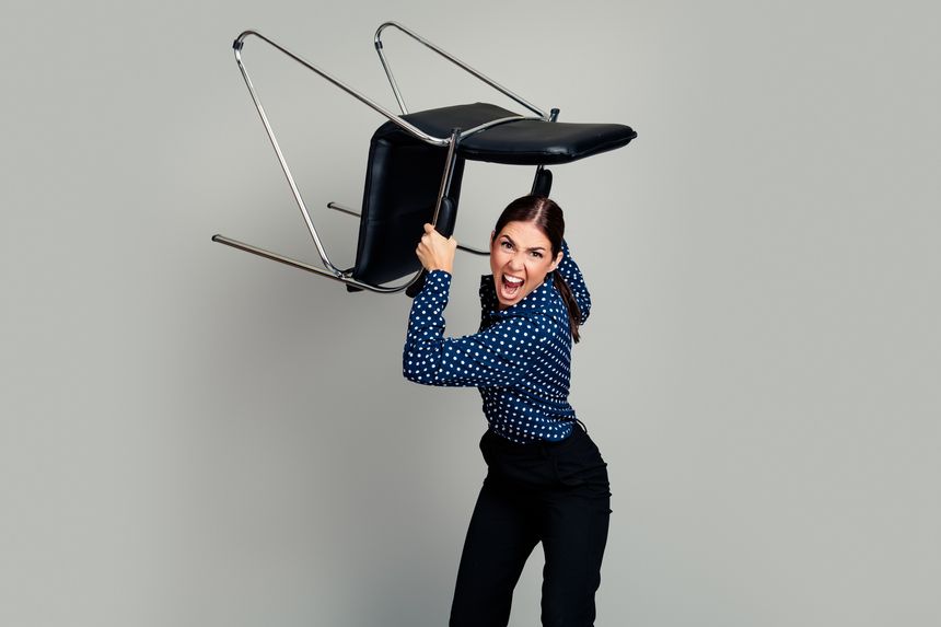 Fierce businesswoman lifts and swings a chair in an office, expressing anger, frustration and stress during a heated outburst. Dramatic emotion, workplace conflict and intense body language captured mid-action.