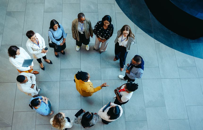 An arial view of a group of new hires standing together during an orientation session in a spacious, modern lobby. The scene conveys a sense of community among a diverse group of professionals.
