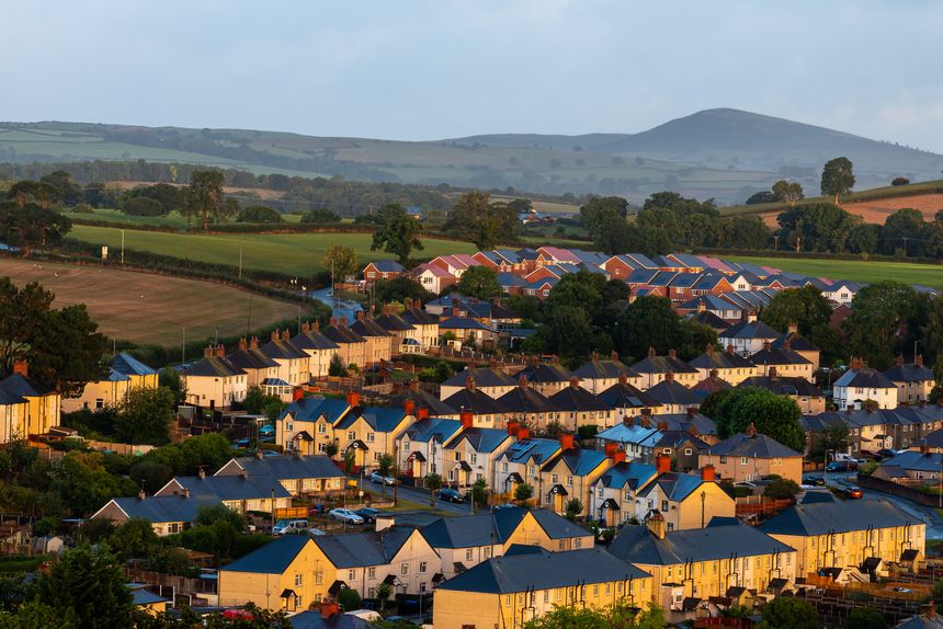 Rows of houses in Denbigh illuminated by warm early morning light, with rolling fields and distant hills forming a rural backdrop