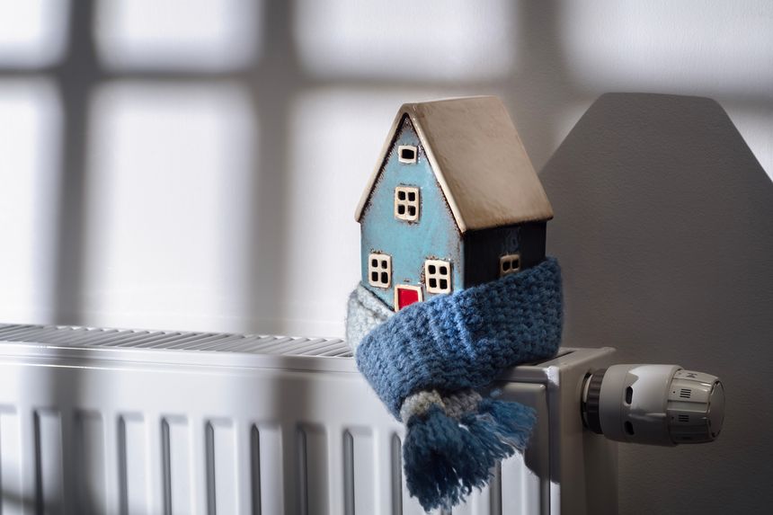 House model wrapped in scarf on radiator home winter heating and insulation background fuel and energy crisis concept