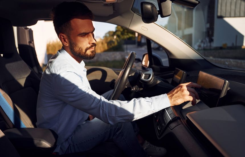 Man is sitting in the vehicle. Young stylish guy is with electric car at daytime.