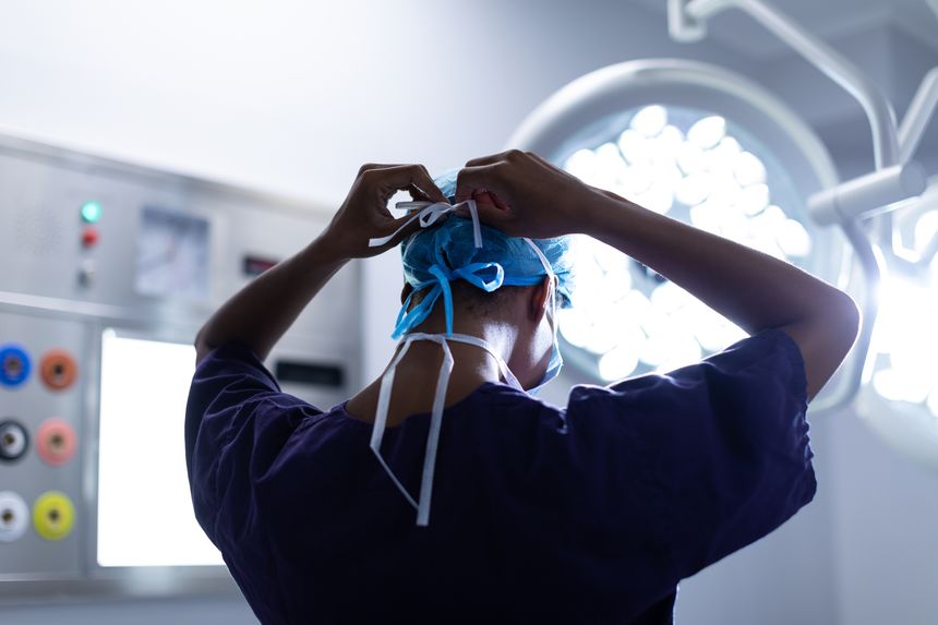 Rear view of Mixed-race female surgeon wearing surgical mask in operation theater at hospital