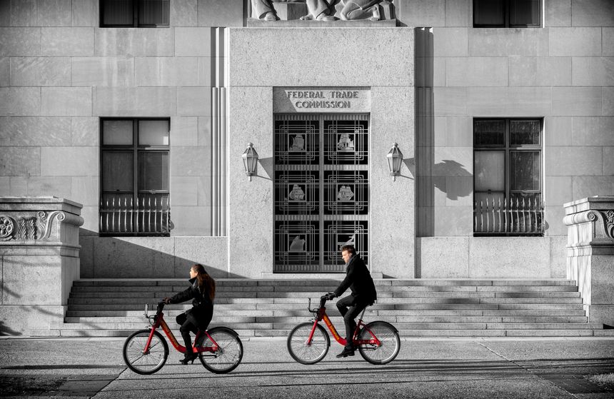 Two bicyclists, using bicycles from a bike sharing system, ride past the Art Deco Federal Trade Commission (FTC) building in Washington DC