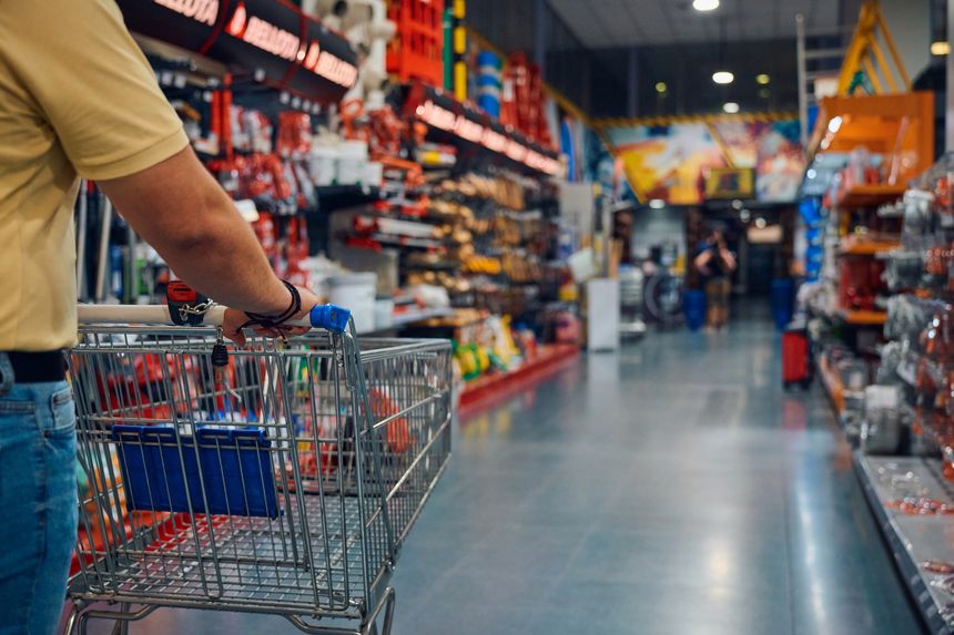 A man navigates through a retail store aisle, pushing a shopping cart filled with varied tools.