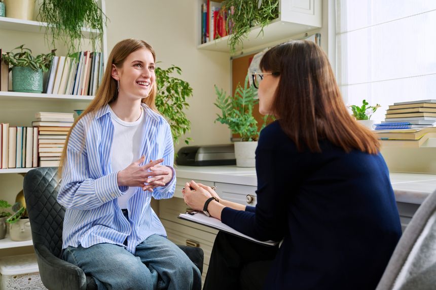 Smiling positive young teen female patient talking to professional mental therapist. Teenager girl high school college student in therapy with psychologist psychotherapist counselor. Treatment support