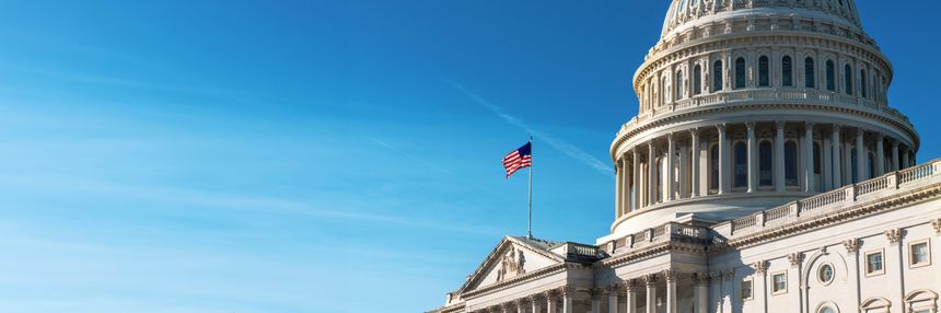 Panoramic view of the United States Capitol dome with its flag against a blue sky.