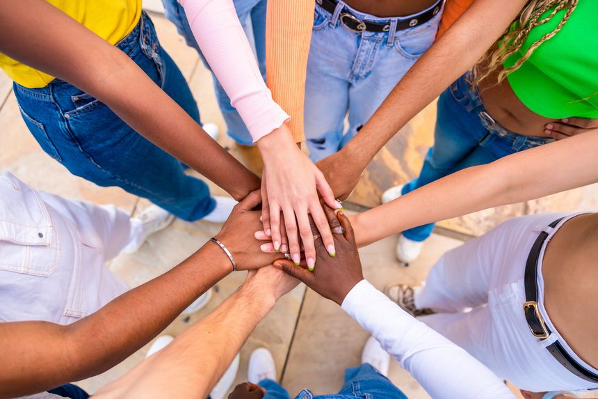 Top view close-up photo of multi-ethnic young people joining hands in a huddle