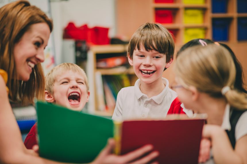Teacher is sitting in the classroom with her primary school students, reading a story to them.