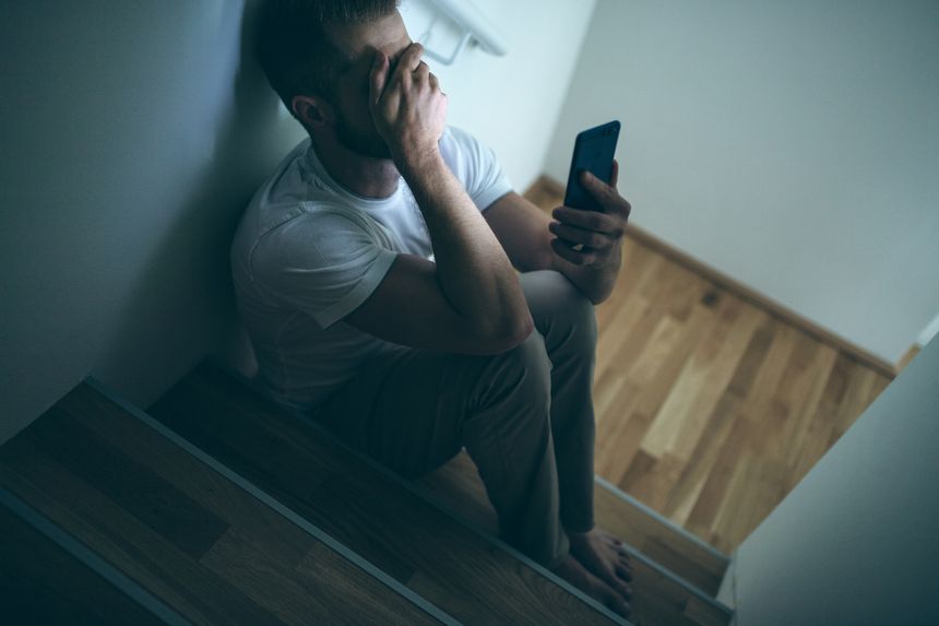 Depressed man sitting in the dark with his smartphone