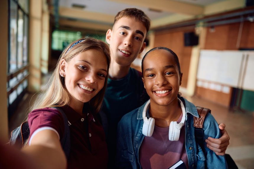 Happy teenagers taking selfie at high school and looking at camera.