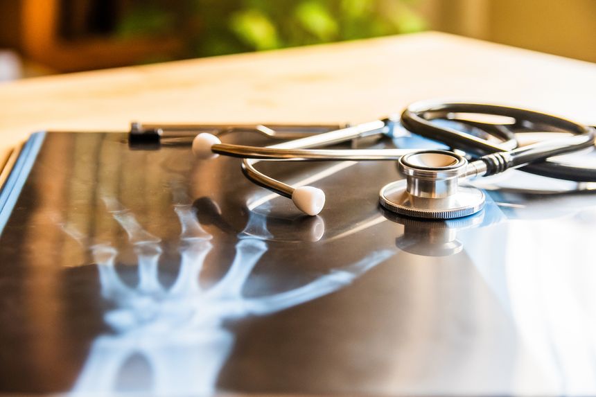 Stethoscope is resting on x-ray image of a human hand on a doctor's desk, suggesting concepts of healthcare, medical diagnosis, and potential work-related injury