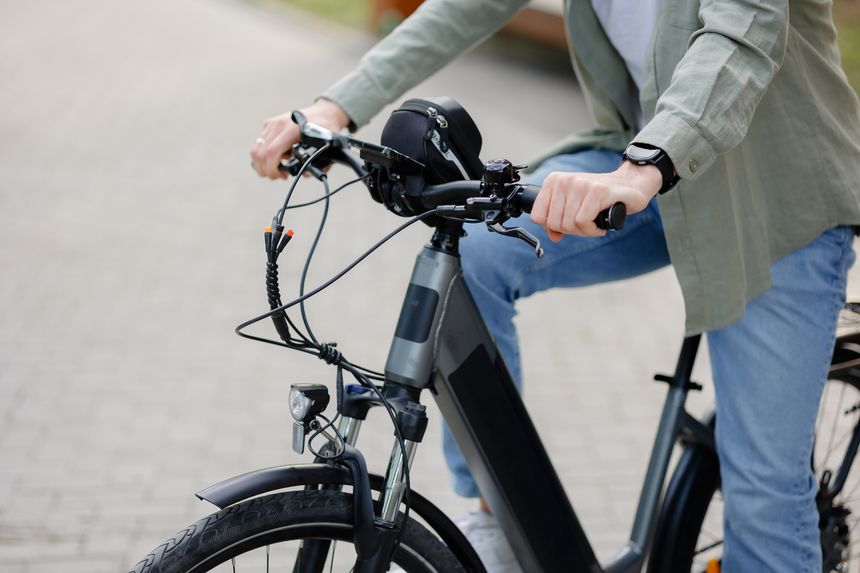 A person in casual attire is riding an electric bike along a well-maintained brick pathway in a park. The scene captures a sunny day, promoting outdoor activities and healthy living.