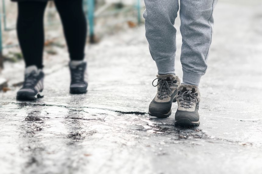 Pedestrians glide along the icy sidewalk. Winter ice on footpaths.