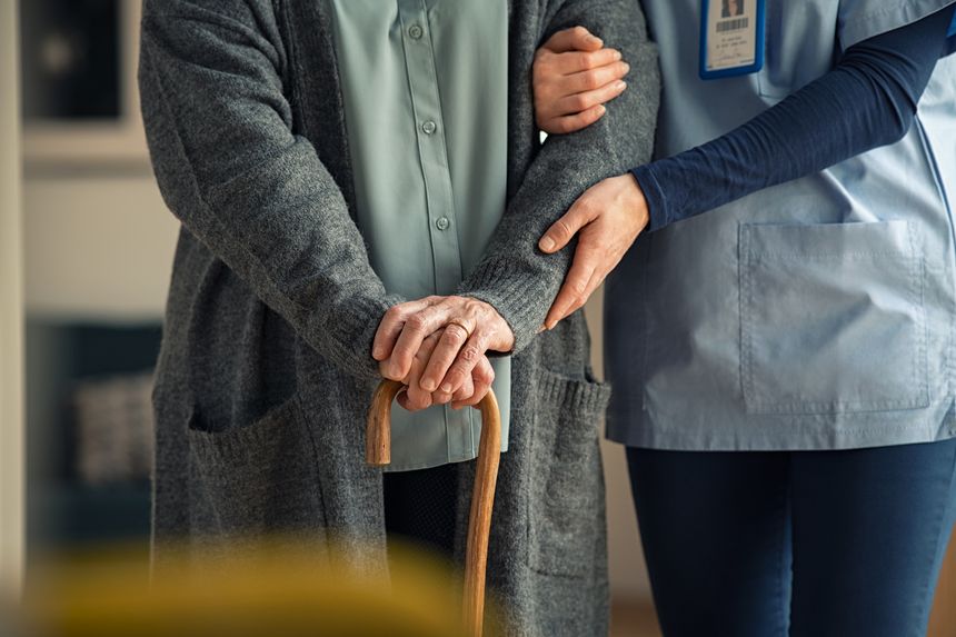 Close up hands of caregiver doctor helping old woman at private clinic. Close up of hands of nurse holding a senior patient with walking stick. Elder woman using walking cane at nursing home with nurse holding hand for support.