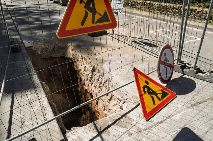 Deep trench along city street surrounded by safety fence and warning signs, concept of road construction, repair and infrastructure safety.
