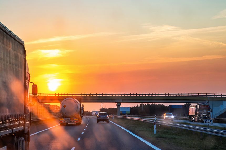 Highway traffic during sunset with trucks and cars through a dirty windshield, showcasing transportation, logistics, road safety and the challenges of visibility while driving on long journeys.