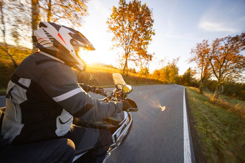 Driver riding motorcycle on empty mountain road during sunset