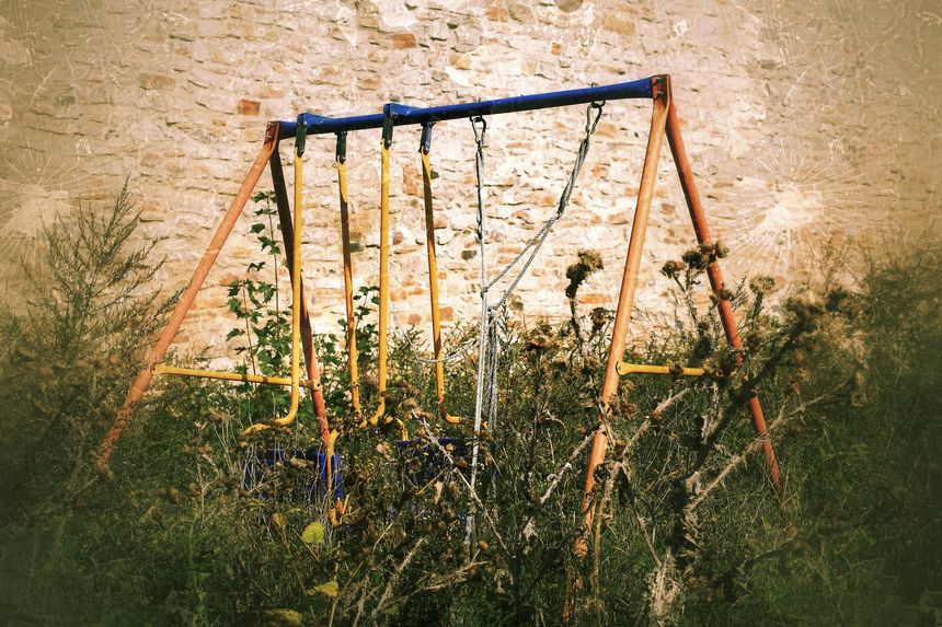 Abandoned swing in thistles in scary, grungy image.