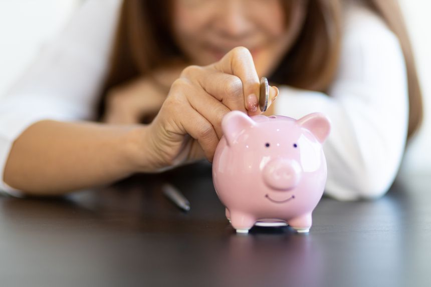 Close-up woman putting coin in piggy bank. Money saving concept.