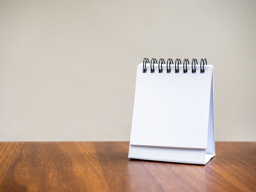 Blank page of desk spiral calendar for organizer concept to plan and reminder, standing on wooden table and grey background. Mock up small table calendar paper, front view, template photo for design.