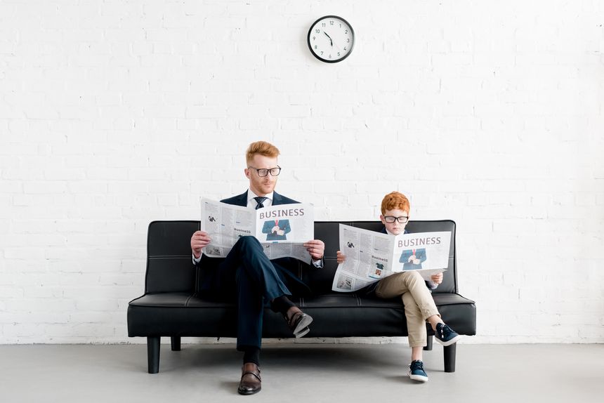father and son businessmen wearing eyeglasses and reading newspapers on sofa