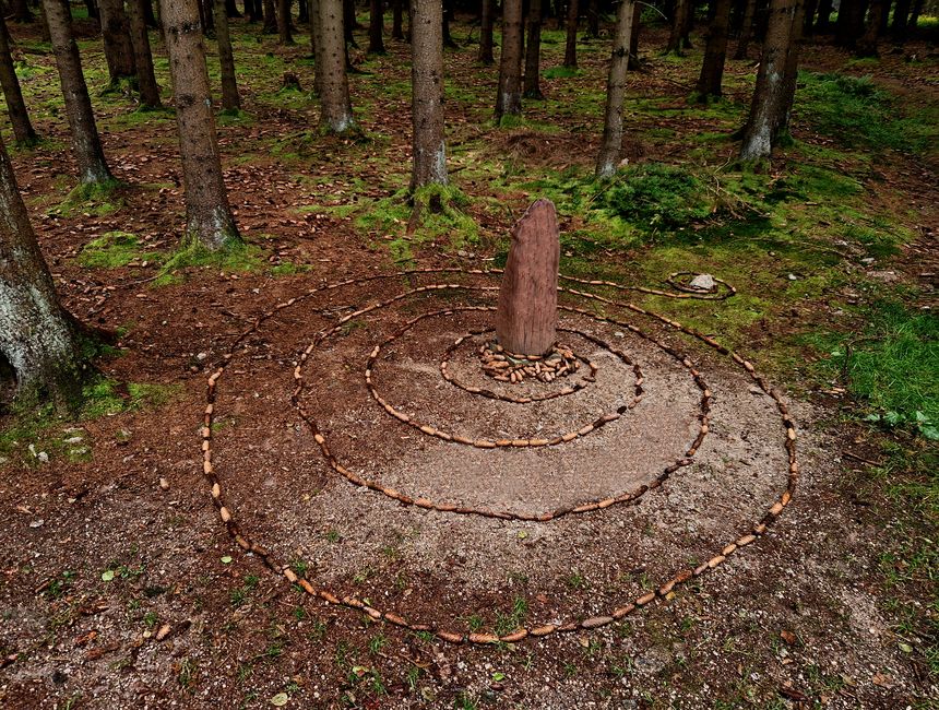 A spiral of pine cones around a wooden menhir. A children's game turned into tasteful land art